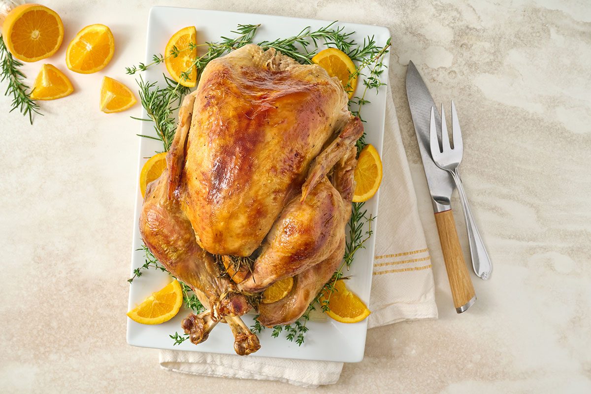 Overhead hero shot of the finished Taste of Home Orange Turkey, golden brown and garnished with fresh orange wedges and herbs on a serving platter.