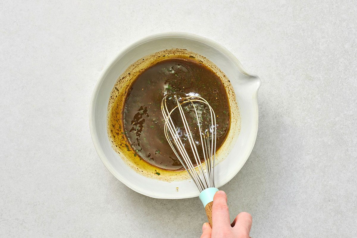 Whisking olive oil, vinegar, pesto, salt, and pepper in a small bowl 