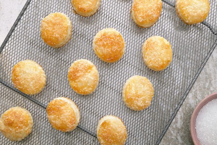 overhead shot of a baking rack filled with golden-Puff pastries sprinkled with sugar crystals, a bowl of sugar crystals sits beside the rack