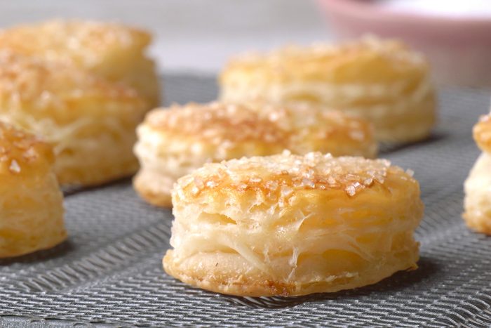 closeup shot of a baking rack filled with golden-Puff pastries sprinkled with sugar crystals, a bowl of sugar crystals sits beside the rack