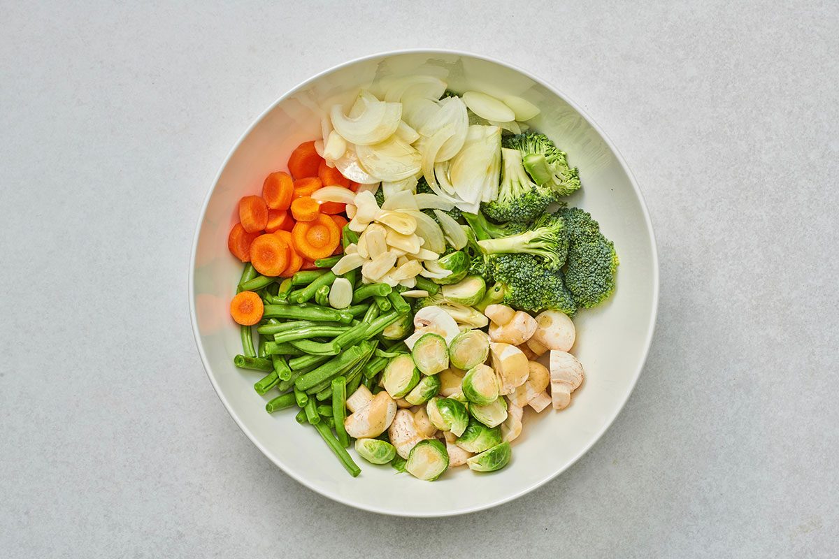 In a large bowl, combined green beans, broccoli, mushrooms, Brussels sprouts, carrots, onion, and garlic