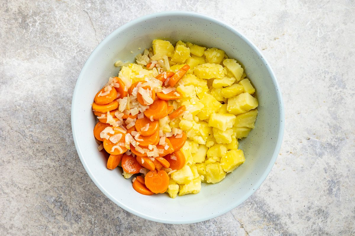 Taste of Home Russian Potato Salad recipe photo of the cooked potatoes in a bowl topped with cooked carrots and onion.