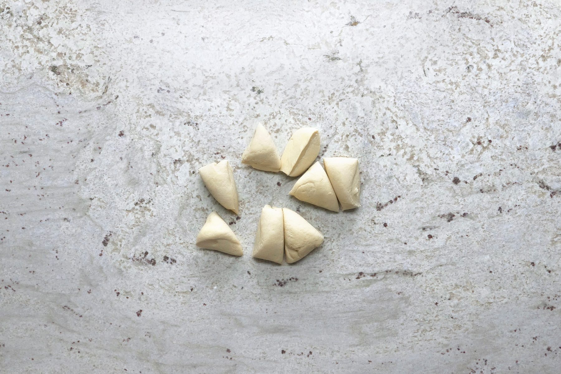 Dough being sliced into small pieces on a marble surface.