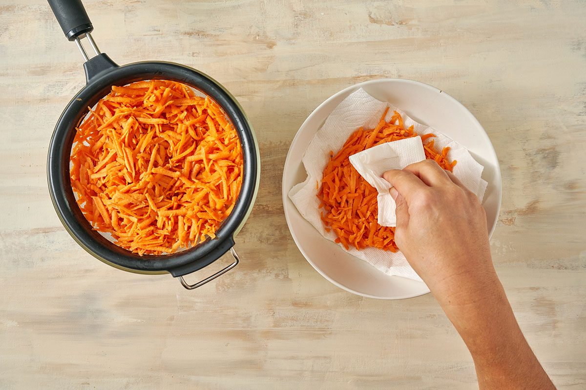 Overhead view of shredded sweet potatoes in a a colander draining and patting dry for the Taste of Home Sweet Potato Fritters recipe.