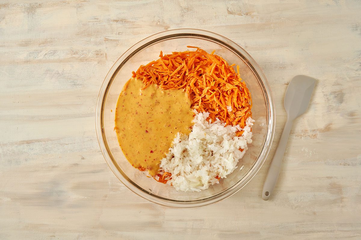 Overhead view of batter, sweet potatoes and onions in large bowl for the Taste of Home Sweet Potato Fritters recipe.