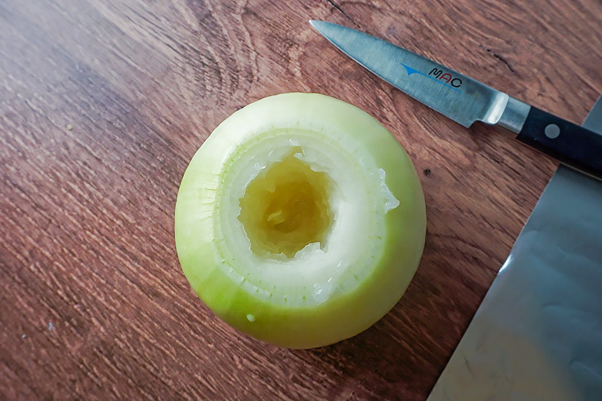 A peeled and cored apple sits on a wooden surface next to a knife with a black handle.