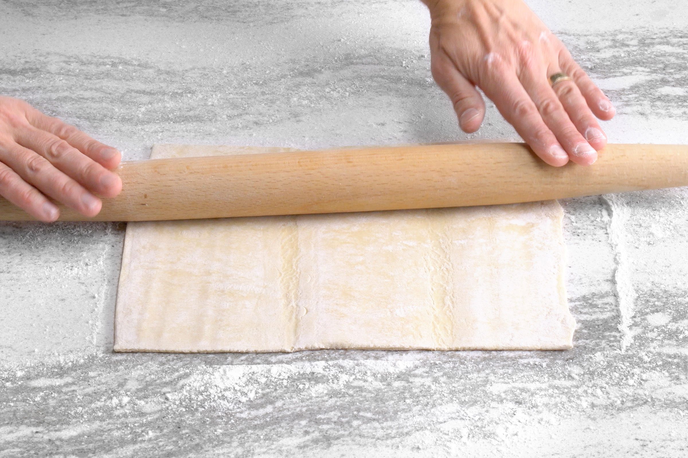Rolling pastry dough sheet using a rolling pin on a floured surface