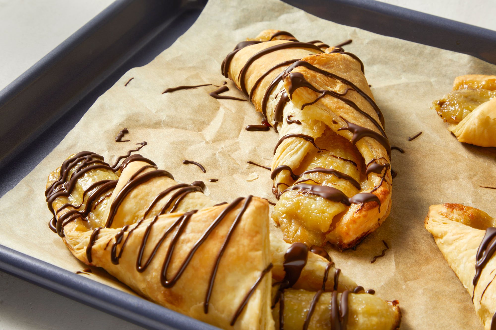 Banana And Chocolate Puff Pastry served in a tray with chocolate syrup spread over it 