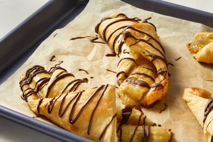 Banana And Chocolate Puff Pastry served in a tray with chocolate syrup spread over it
