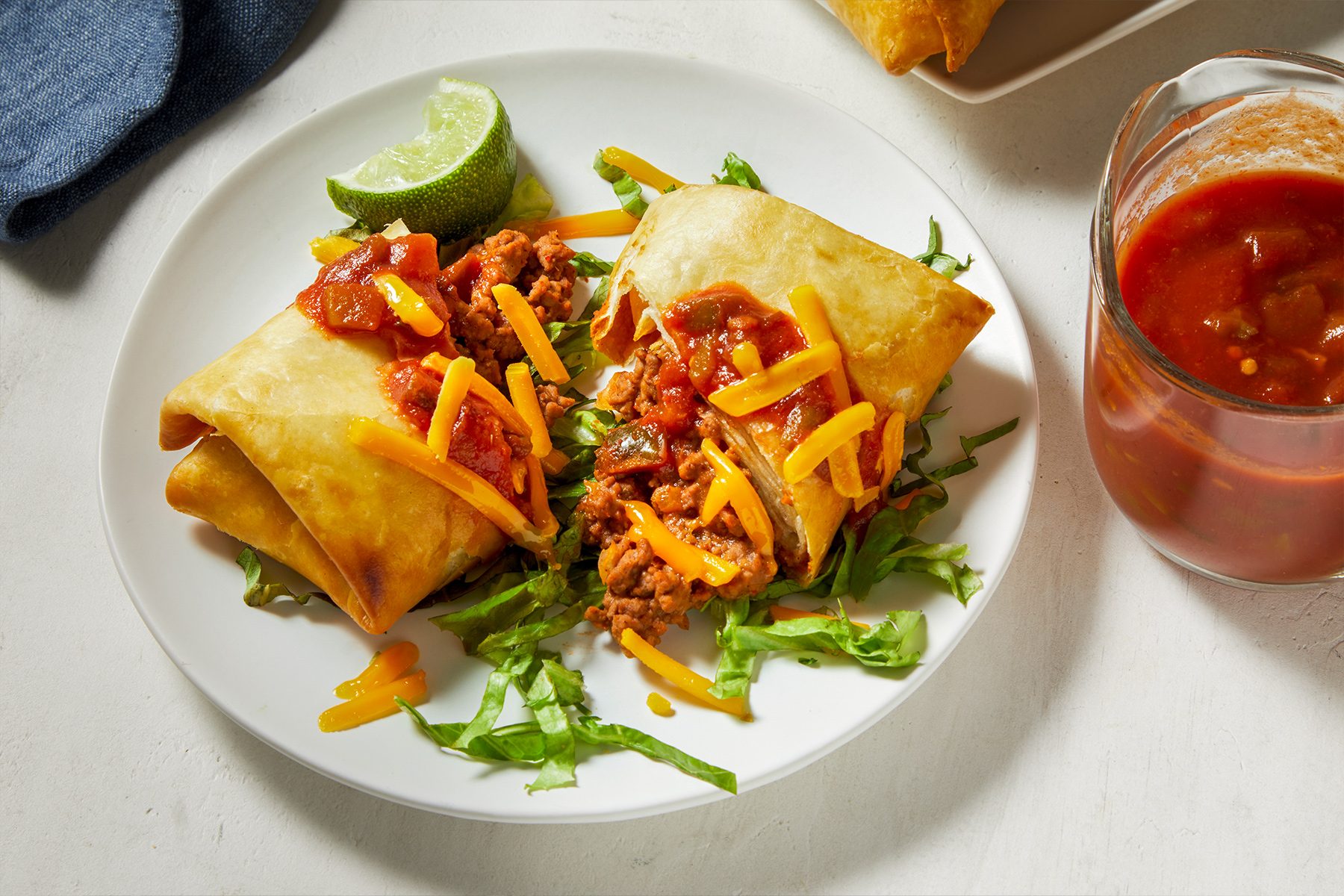 A plate filled with chimichangas topped with melted cheese and drizzled with savory sauce.