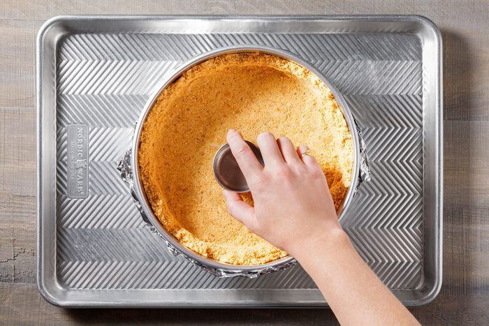 Pressing graham cracker crust to the bottom of the prepared pan for baking