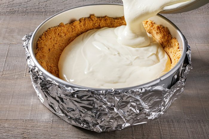 Pouring the creamy cheesecake batter into the cold crust in set at the bottom of the baking pan