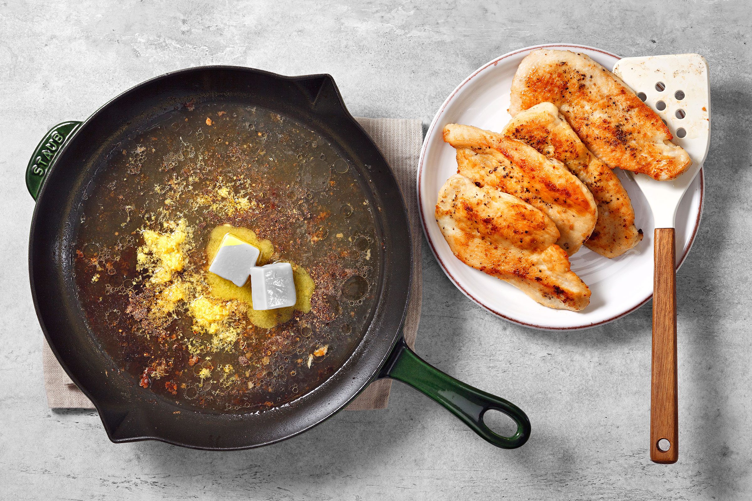 Butter, chicken broth, lemon zest and seasoning in a large skillet with golden brown chicken breasts on the side