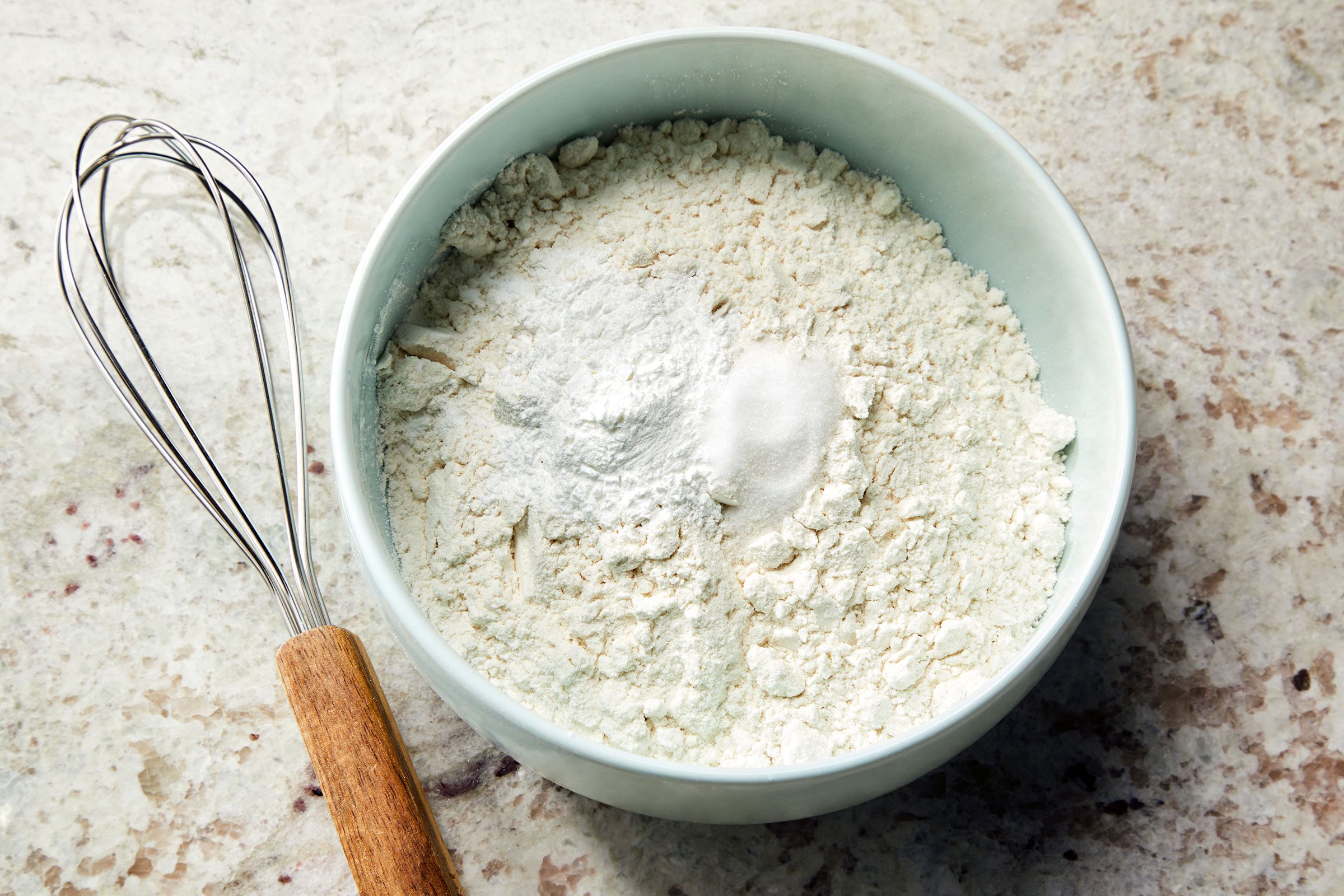 Dry ingredients for lemon olive oil cake in a bowl with a whisker