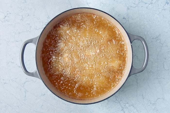 A pot filled with simmering golden-brown oil on a light blue marble surface.