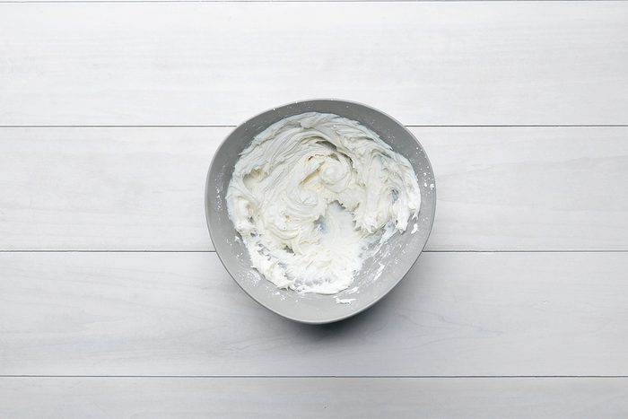 A bowl of whipped cream on a white wooden surface.
