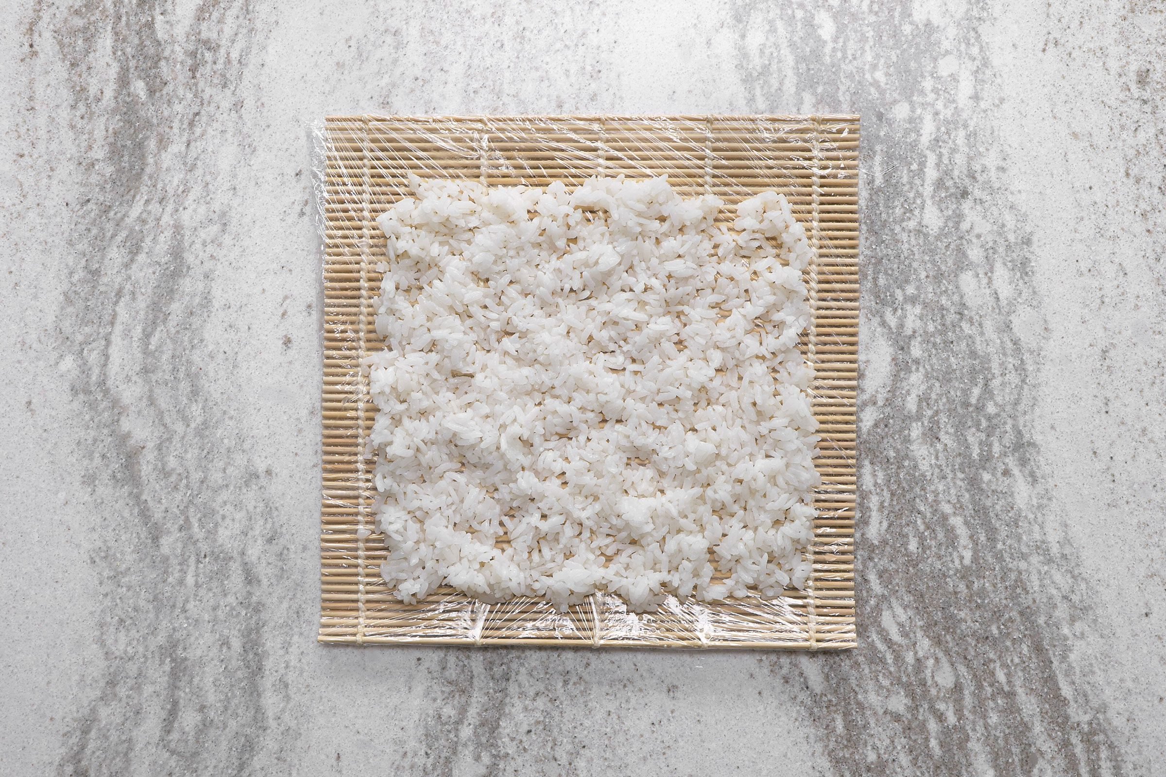 Sushi rice on sushi mat wrapped with plastic wrap