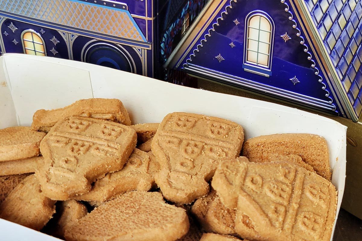 An assortment of light brown speculoos cookies shaped like Dutch houses, with a blue house-shaped box in the background