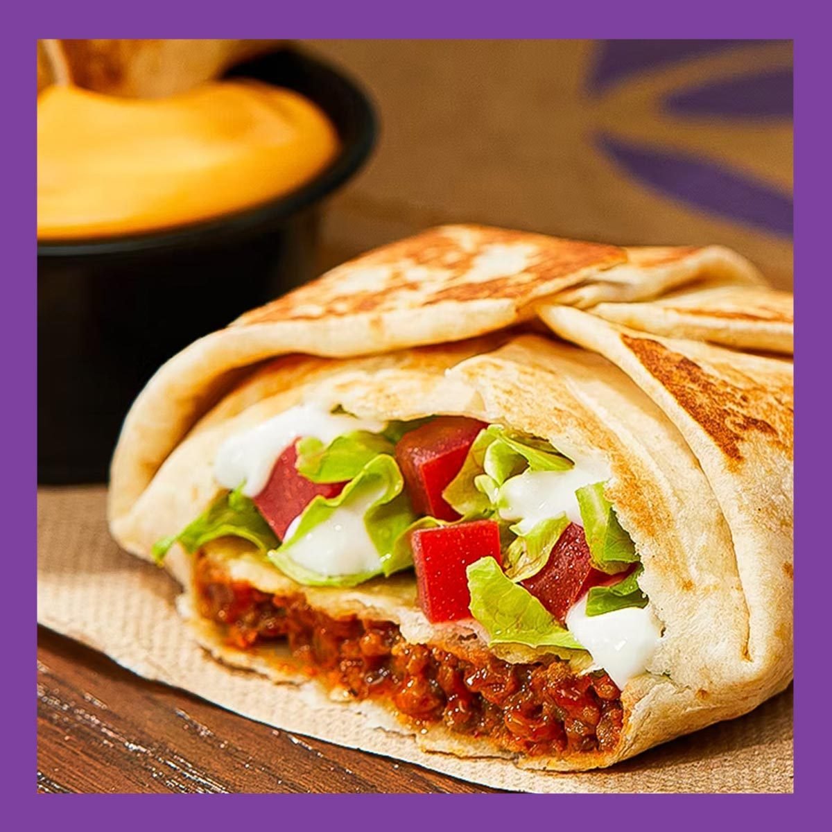 Taco Bell's upcoming Crunchwrap slider on a table, with a cup of queso in the background