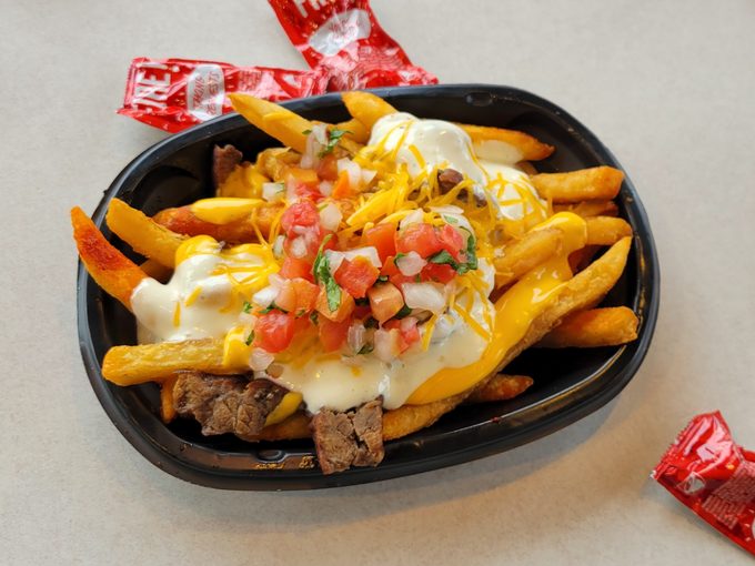 Taco Bell's Steak Garlic Nacho Fries on a table with packets of hot sauce