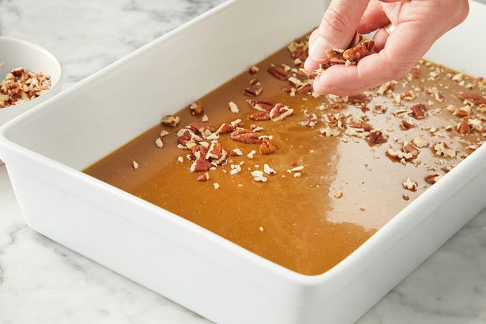 Sprinkling pecans on caramel sauce in a dish