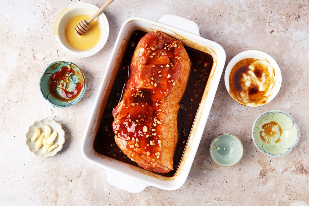Pork shoulder in a marinade in a white baking dish.