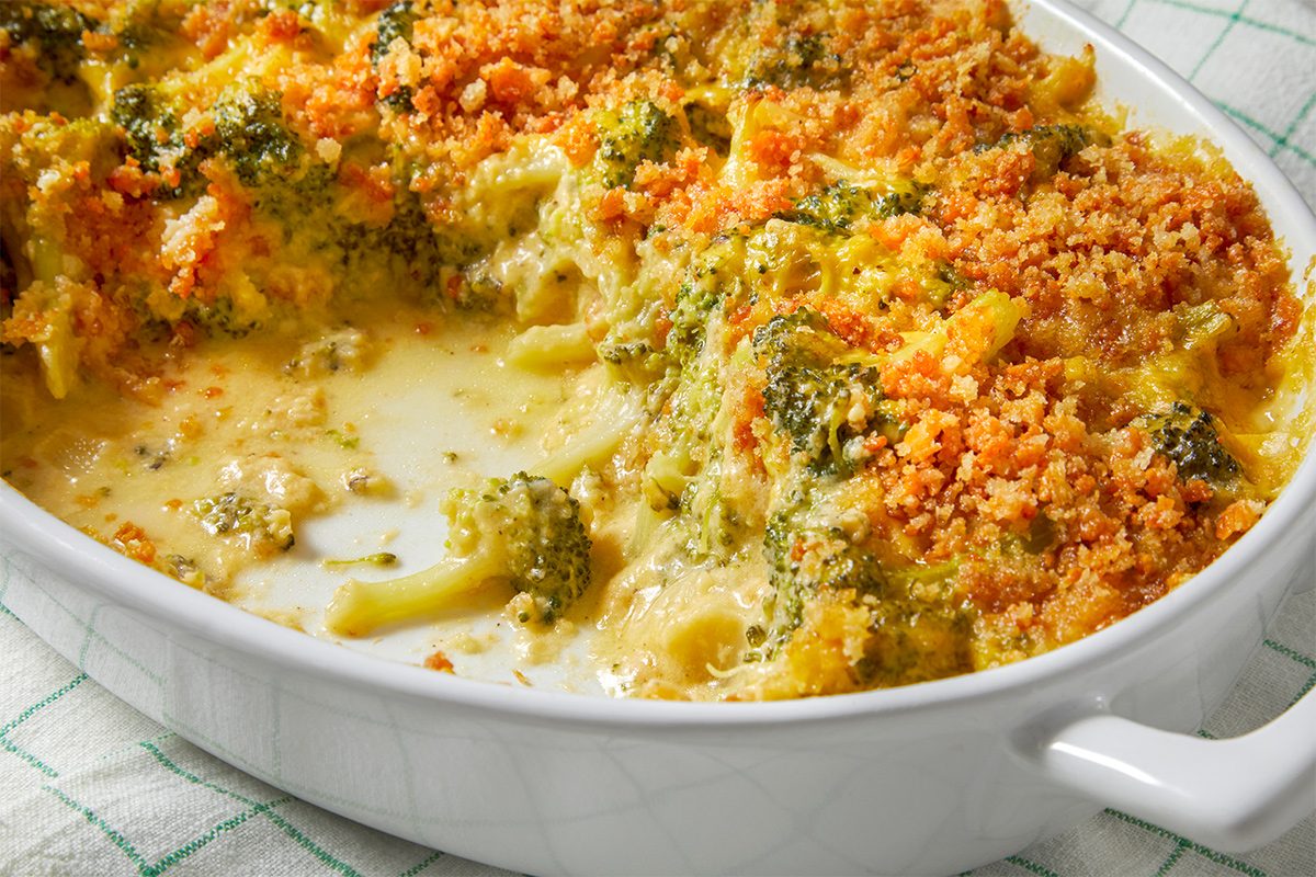 Side view of Cheesy Broccoli Au Gratin kept in a baking dish on a kitchen cloth with some of it taken out.