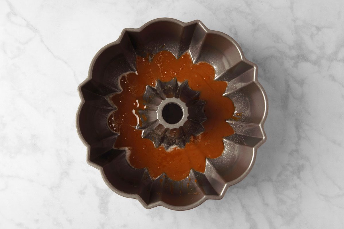 overhead shot of a bundt pan on a white marble countertop; the pan has a brown caramel sauce inside of it