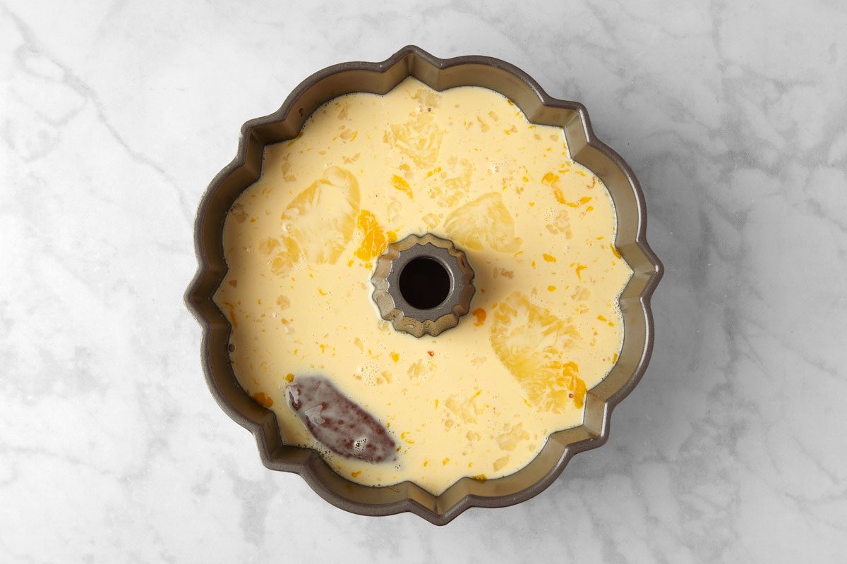 overhead shot of a bundt cake pan on a marble countertop; The pan is filled with a yellow custard-like mixture;