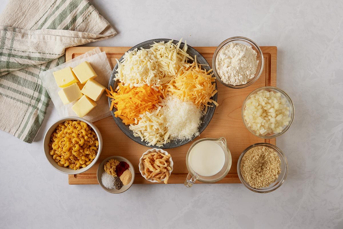 Ingredients for mac and cheese on a cutting board on a counter with a kitchen towel to the top left