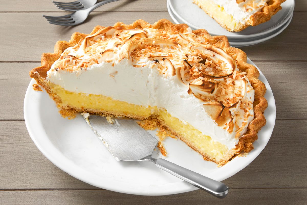 High angle view shot of Favorite Coconut Meringue Pie; in a pie plate; cut slice and serve on small plate; cake knife; forks; wooden surface;