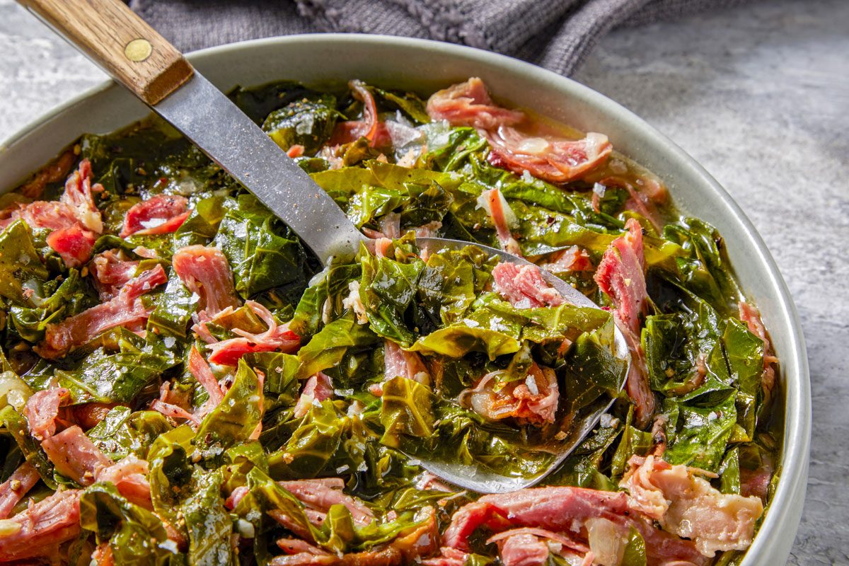 Close shot of Collard Greens with Smoked Turkey; server in a large bowl; serving spoon; napkin; marble surface