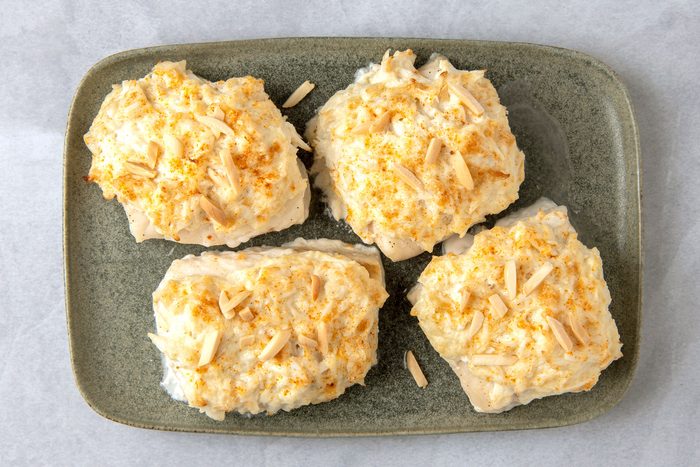 Four pieces of Crab-Topped Fish on a green plate and each piece is topped with a creamy sauce and sliced almonds