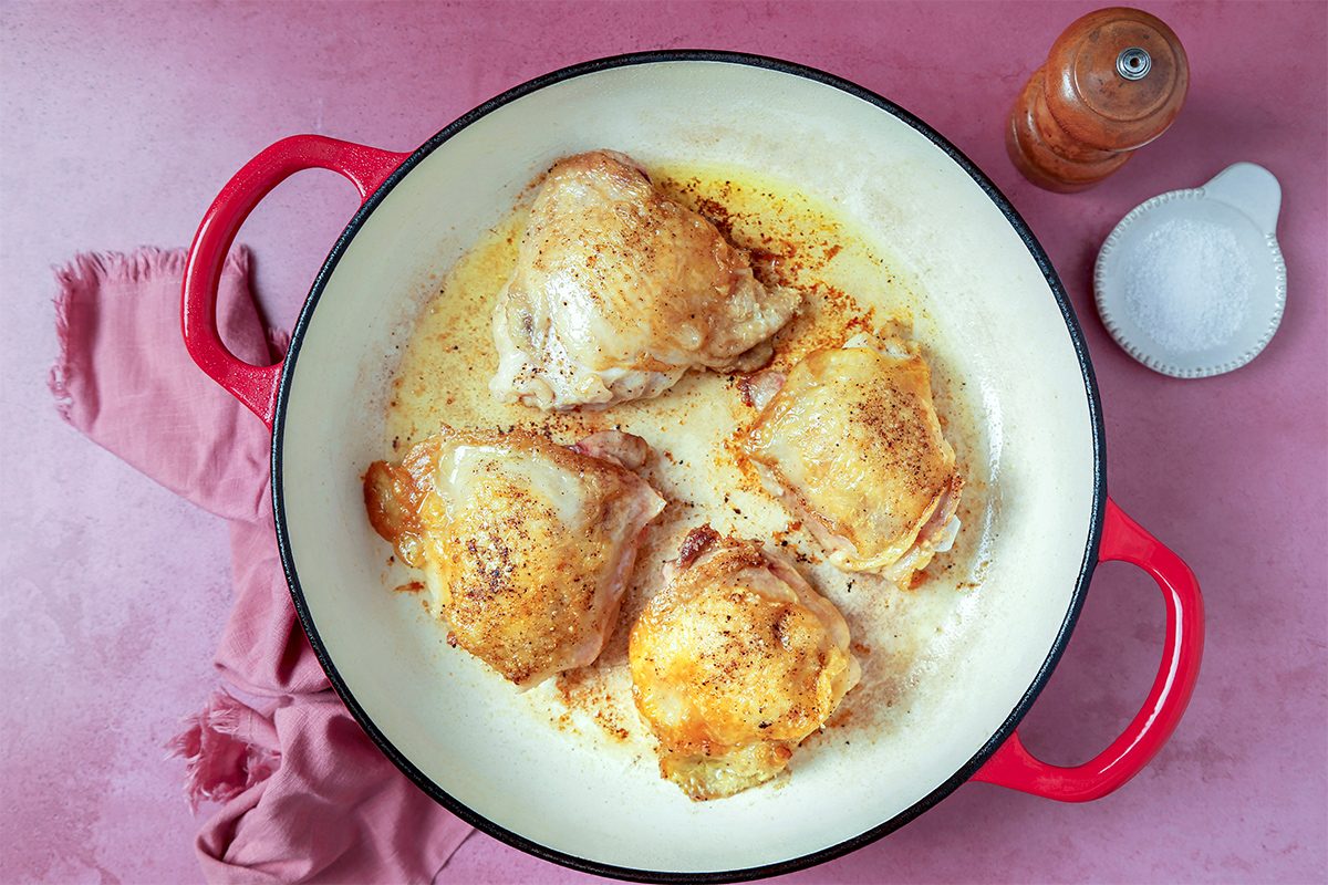 Seasoned chicken thighs browning in a red dutch oven.