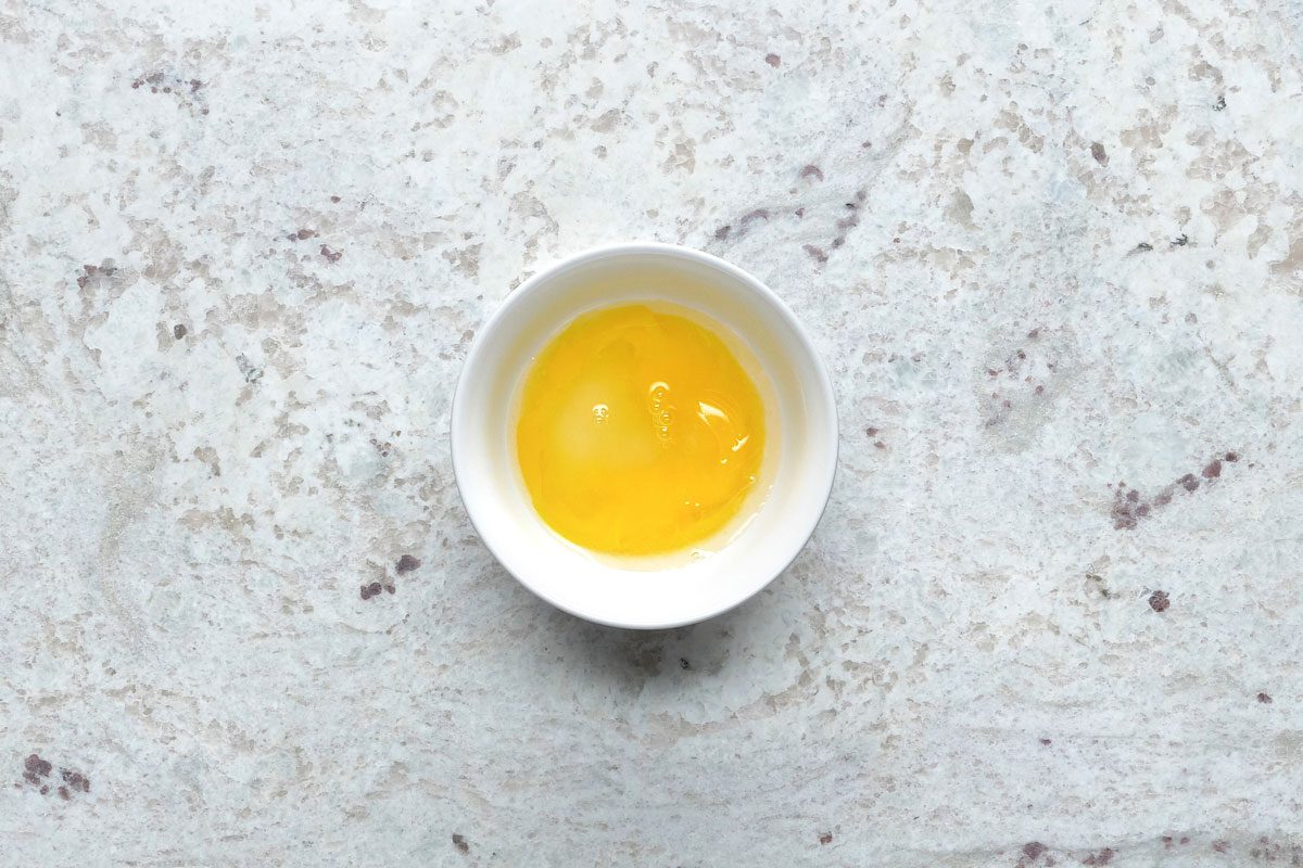 Overhead shot of a small bowl; beat together egg yolk and water; grey surface;