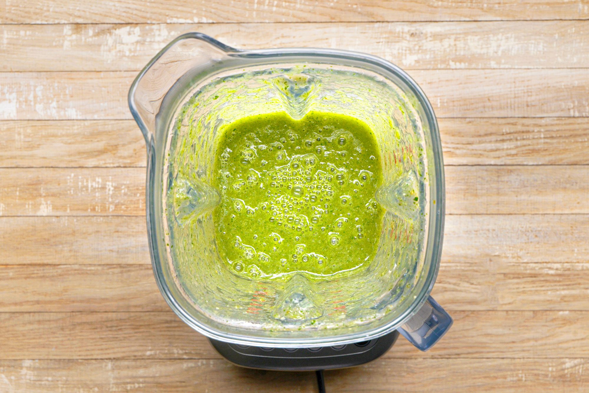 overhead shot of a blender with a green smoothie inside, sitting on a wooden surface