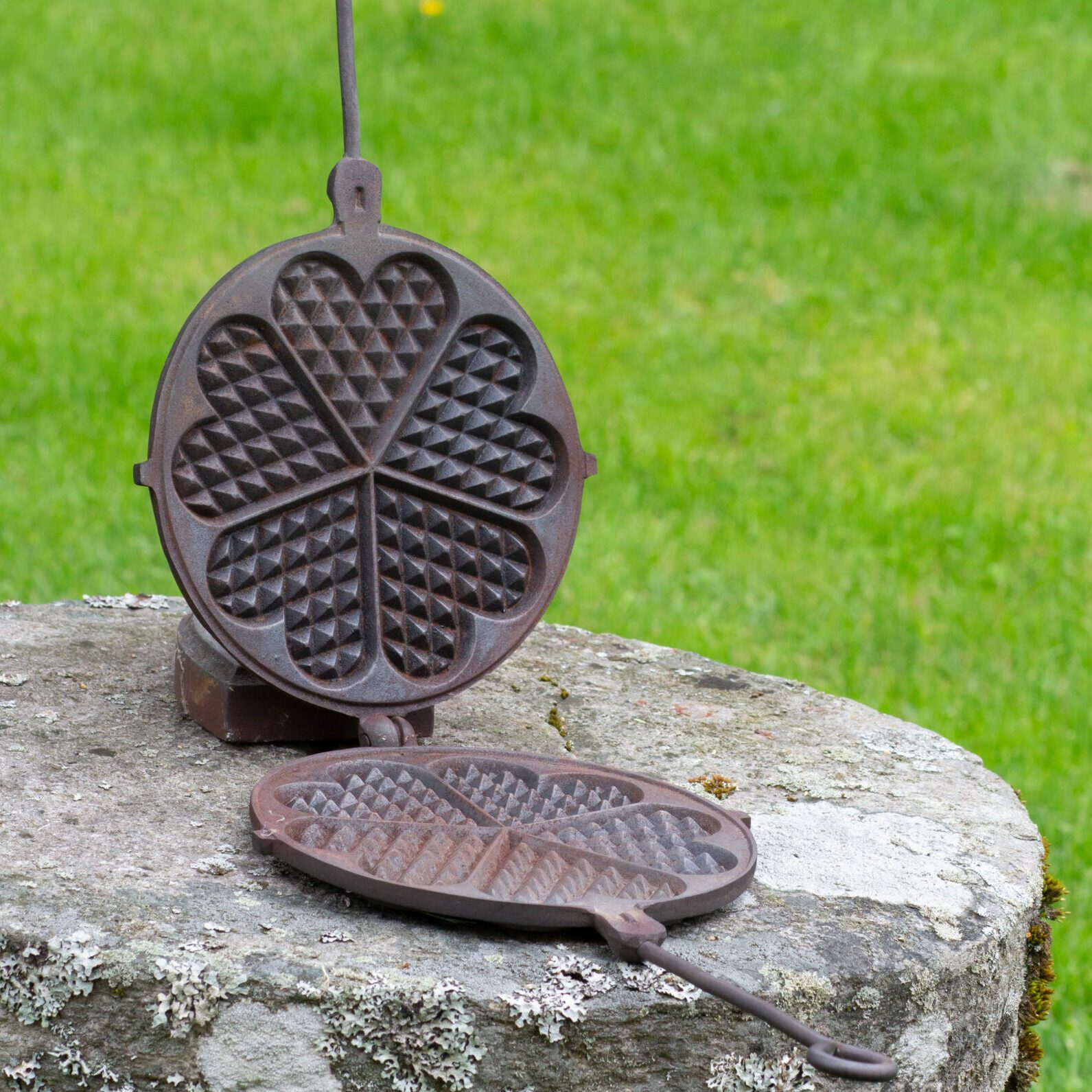 Old waffle iron on a stone stand outside with grass in the background