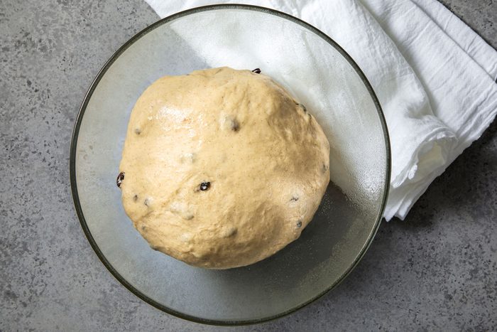 overhead shot of a glass bowl sits on a speckled grey surface, holding a large ball of dough; the bowl is sitting on a white cloth that has been folded in half and placed on top of the surface