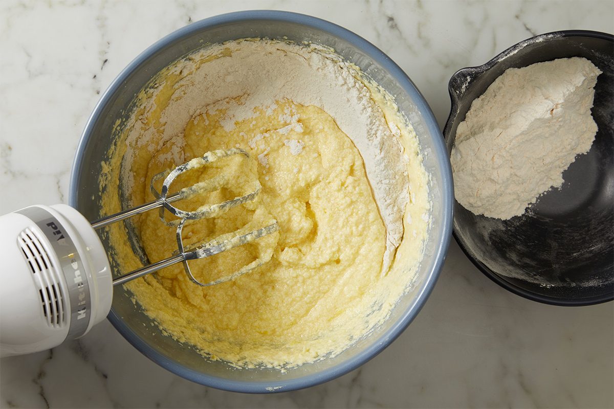 Overhead view of the dry ingredients being whisked into the bowl containing the wet ingredients on a white marble countertop.