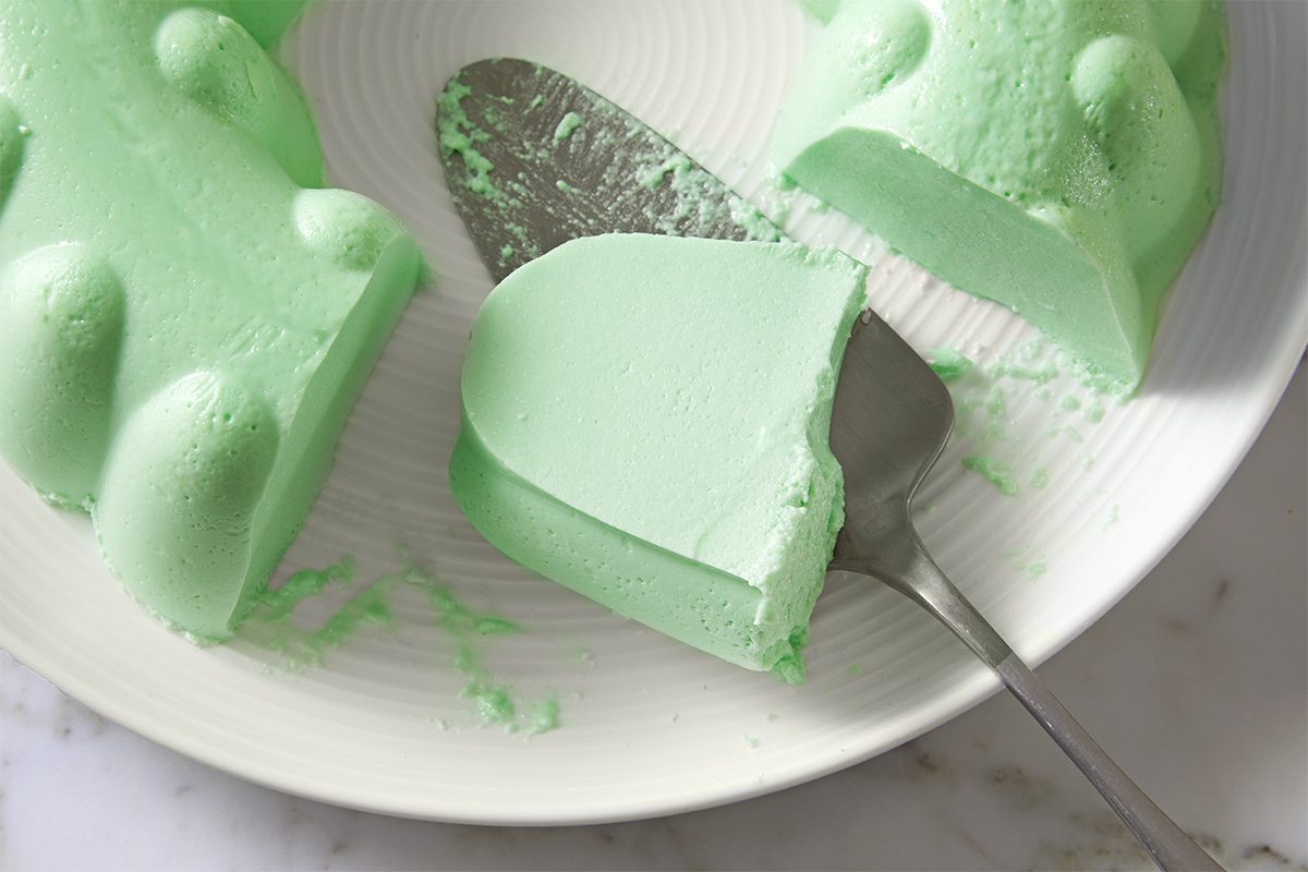 Overhead view of firm lime gelatin salad cut and served with a serving spatula on a white plate kept on top of a white marbletop.