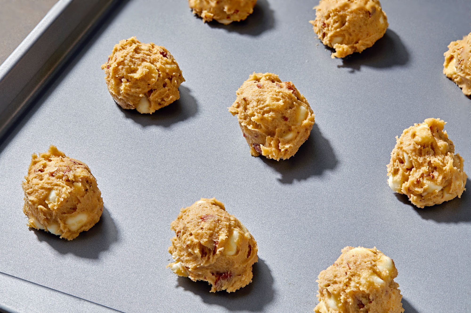 A baking sheet with unbaked cookie dough balls, the baking sheet is gray with a slight metallic finish