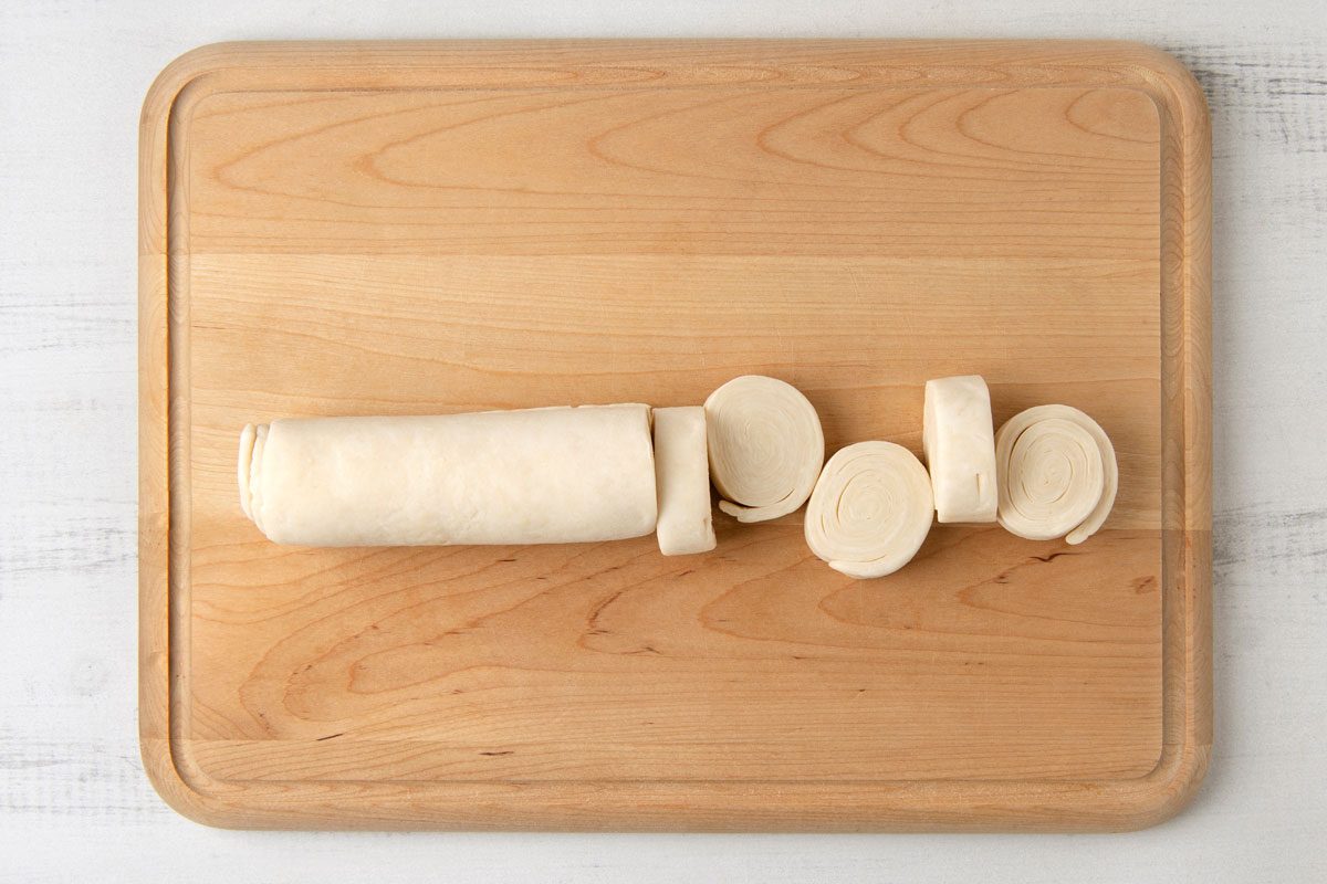 overhead shot of a wooden cutting board with a roll of dough that has been sliced into rounds