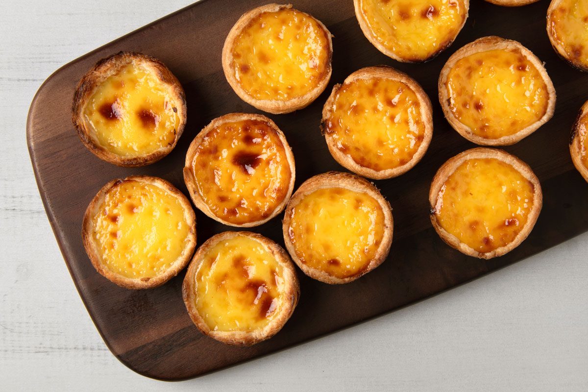 overhead of Portuguese egg tarts, arranged on a wooden board; the background is a light gray