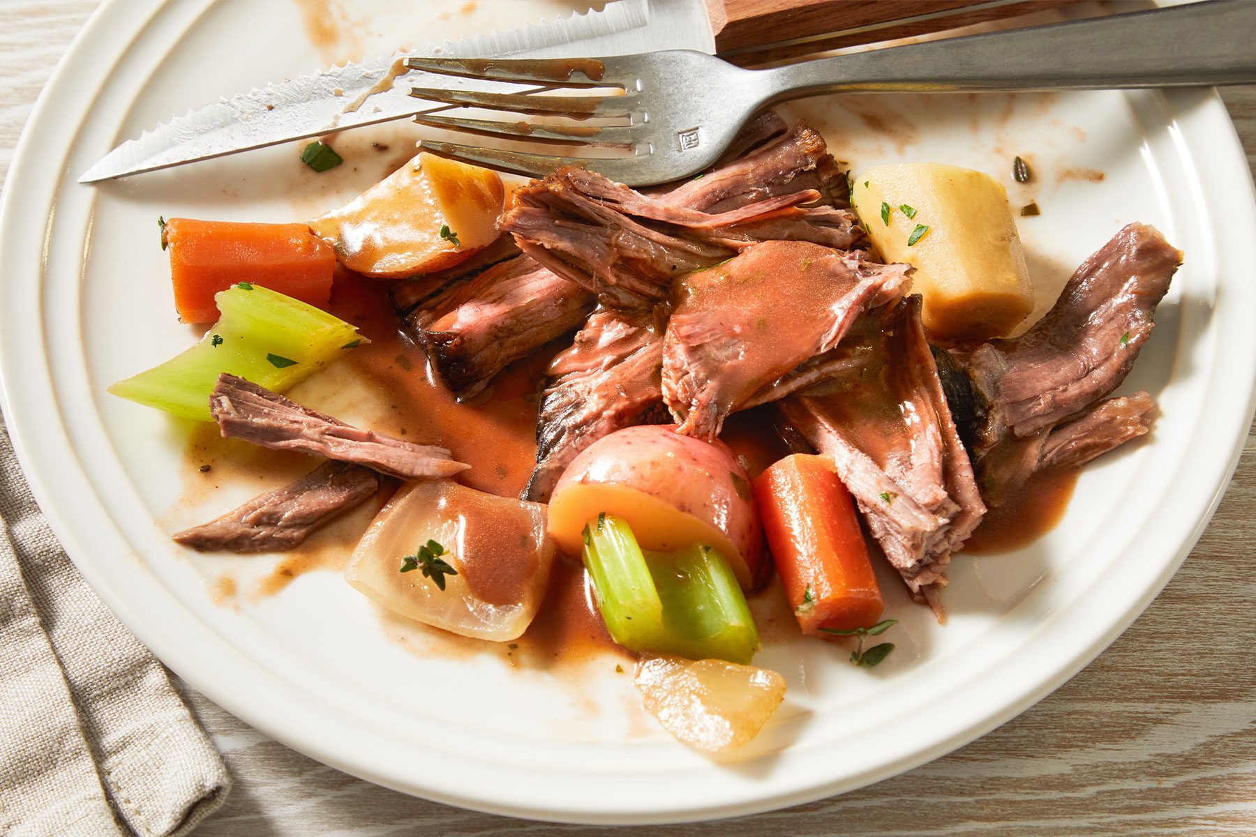 White plate with Pot Roast served with vegetables and sauce