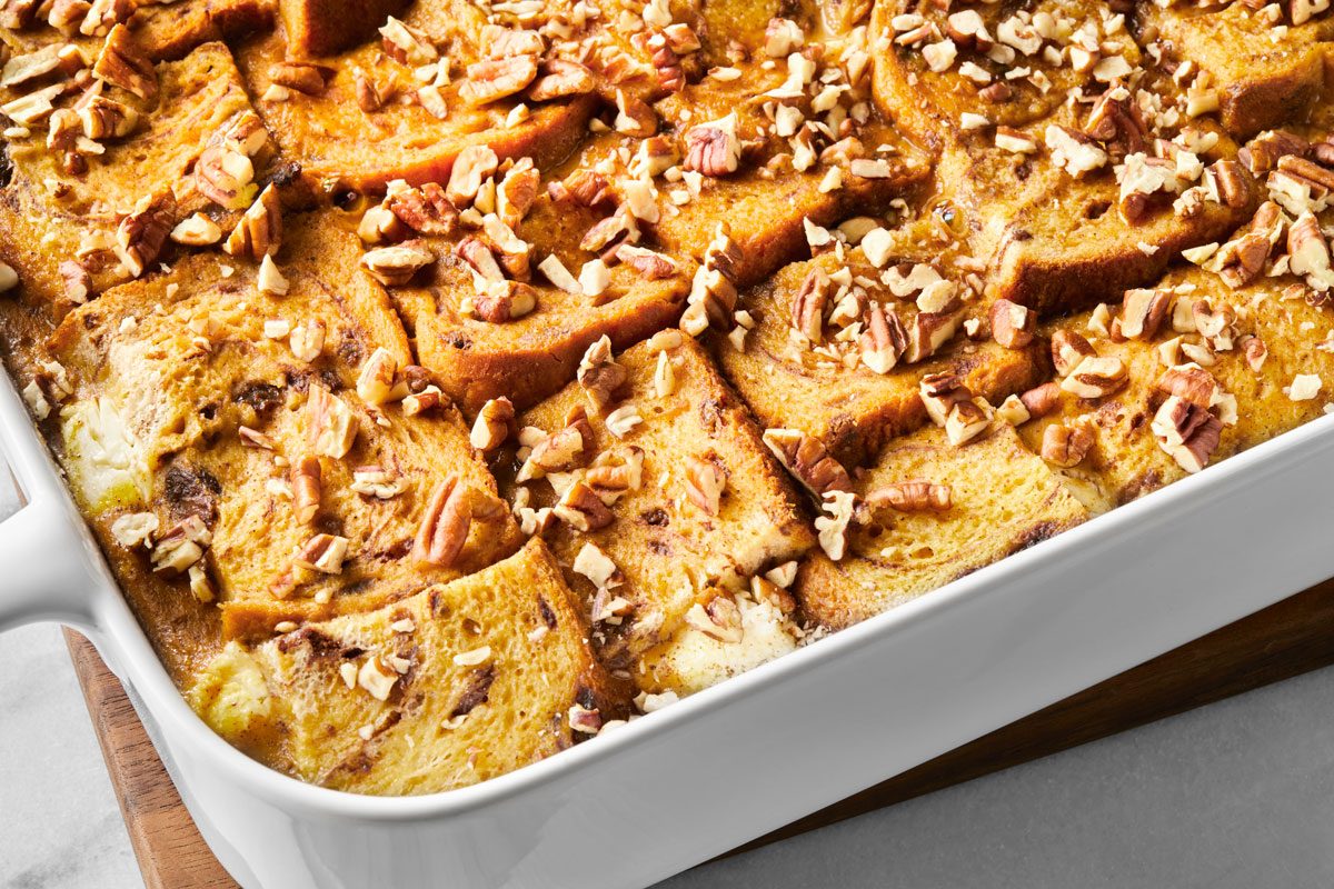 Baked bread pudding topped with pecan nuts in a white baking dish