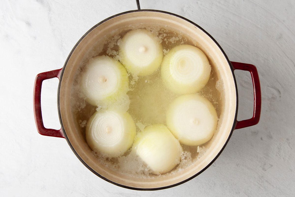 peeled onions being boiled in a dutch oven