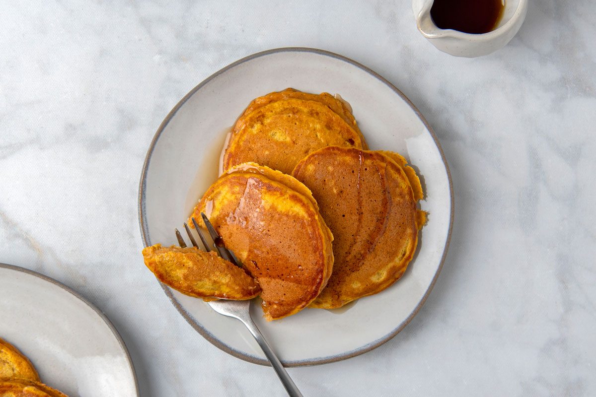 overhead shot of Fluffy Sweet Potato Pancakes; served on plates; with syrup; forks; marble surface;