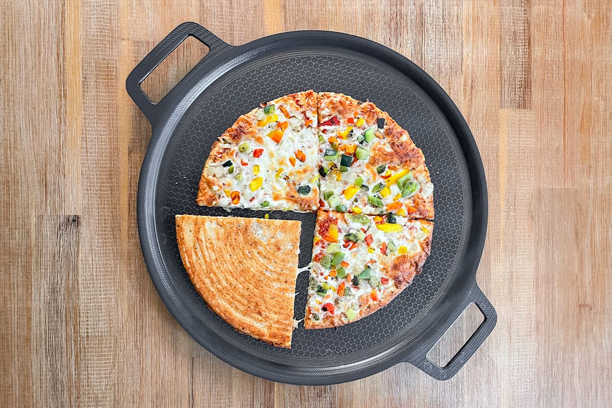 A pizza with various toppings, including green and yellow bell peppers, sits on a black pizza pan. One slice is separated from the main pie, revealing a golden crust. The pan rests on a wooden surface.