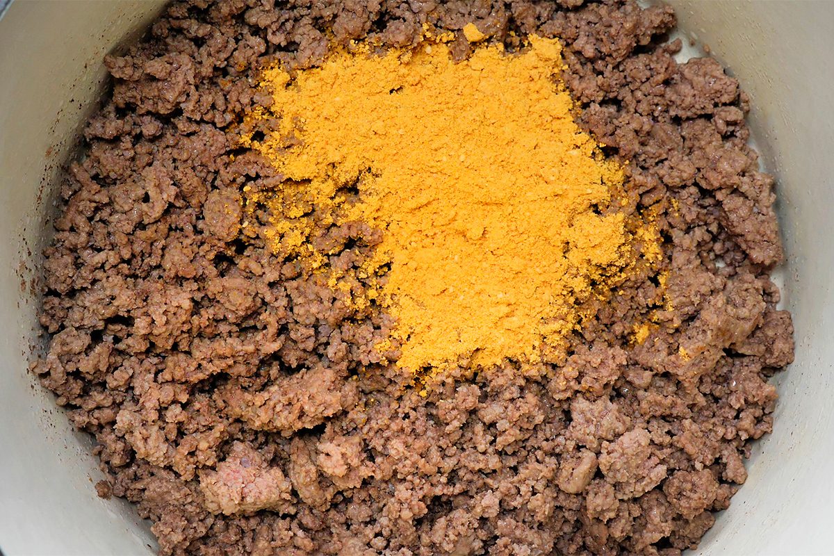 Cooked ground beef with a pile of bright yellow taco seasoning in the center, inside a pot.