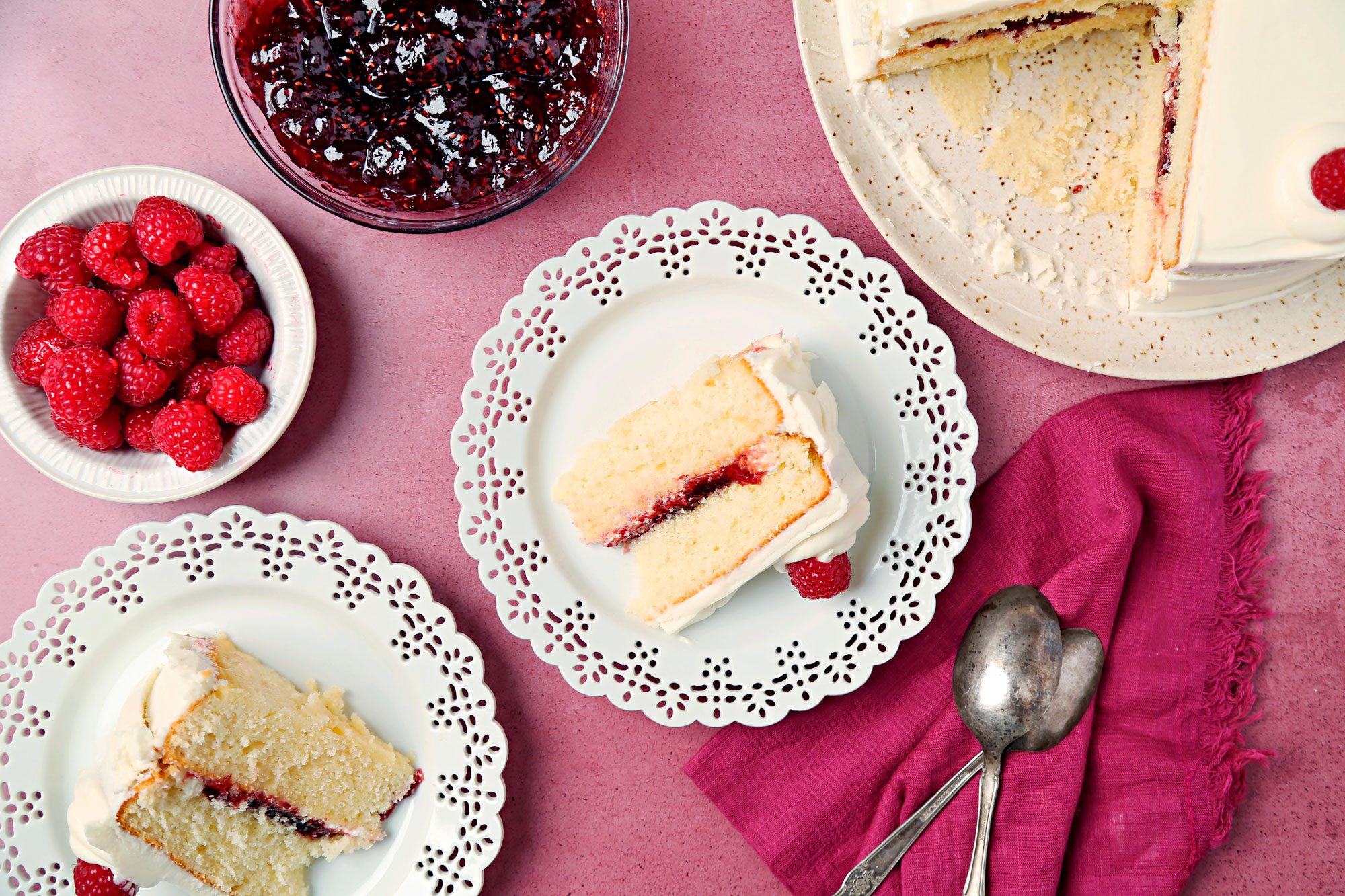White chocolate Raspberry Cake shot on a magenta surface. Cake sliced and served on white lace placed; overhead